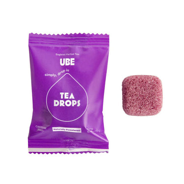 A purple 💜 Ube Tea Drops® packet—a sweet, nutty, & creamy purple delight—rests beside a pinkish-purple, cube-shaped tea drop on a white background.